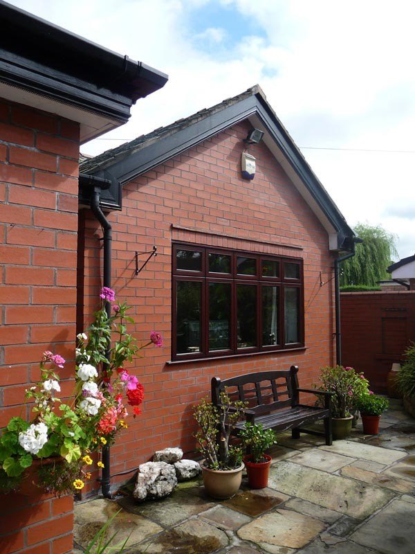 A single-storey brick extension with a hipped roof beside a flagged patio with a bench and flowers