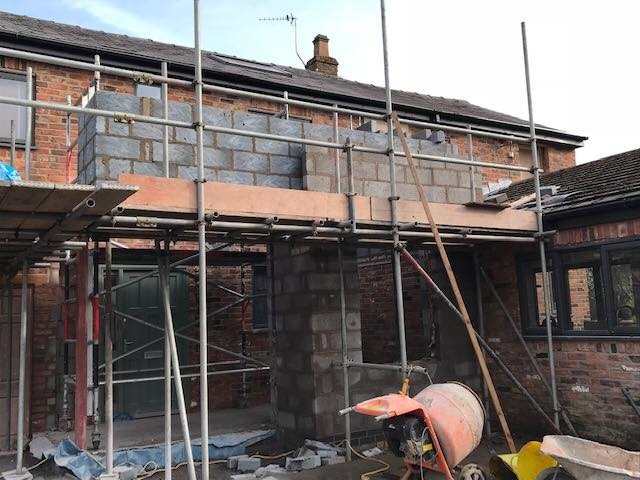 A brick house mid-build with scaffold up and new blockwork above the garages