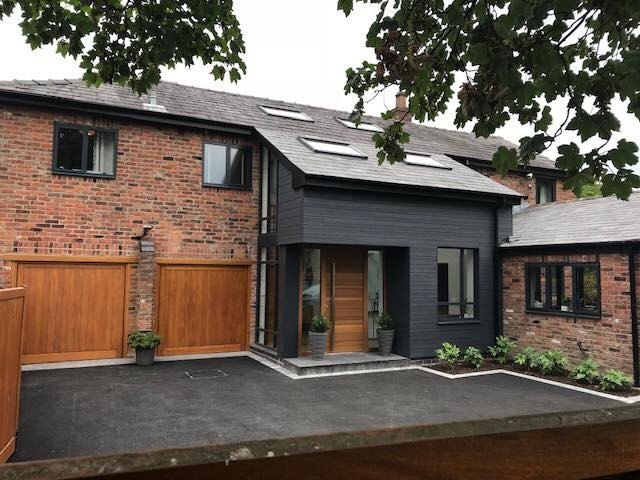 The finished house: a grey-clad two-storey link with rooflights, timber garage doors and a new front door