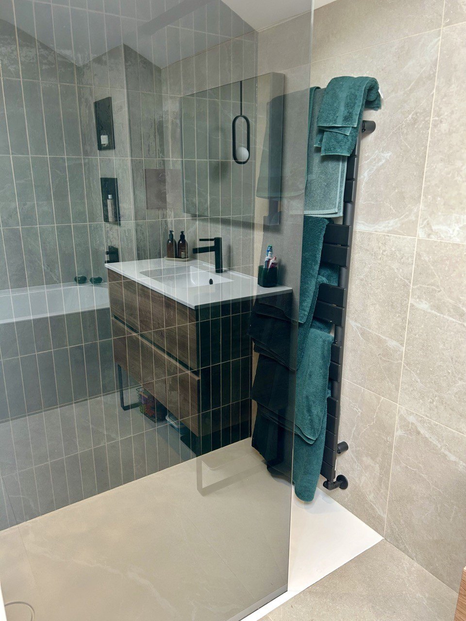 A bathroom finished in large stone-effect tiles with a wall-hung basin, walk-in shower and teal tiled alcove