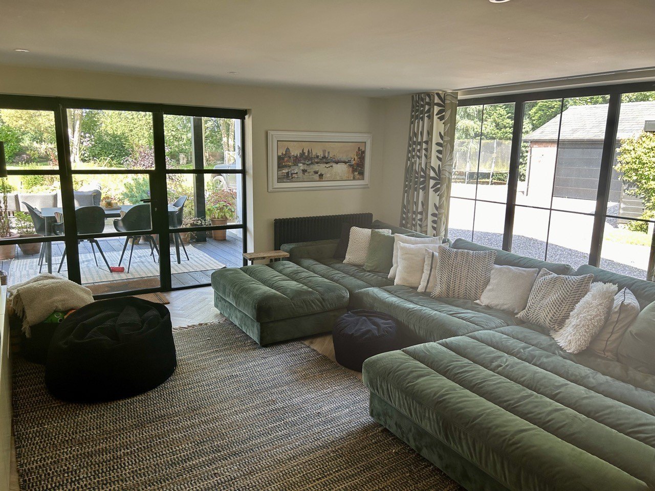 A lounge with a large corner sofa and a wall of black-framed glazing