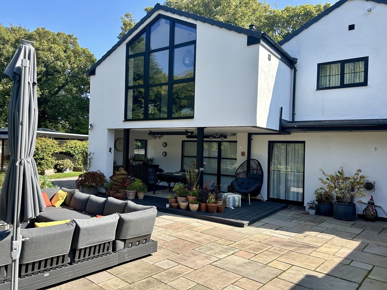 The rear of a white rendered house refurbished by Nyland Construction, with a full-height glazed gable over a paved terrace
