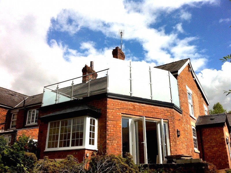 A brick house with a roof terrace and glass balustrade above a bay extension